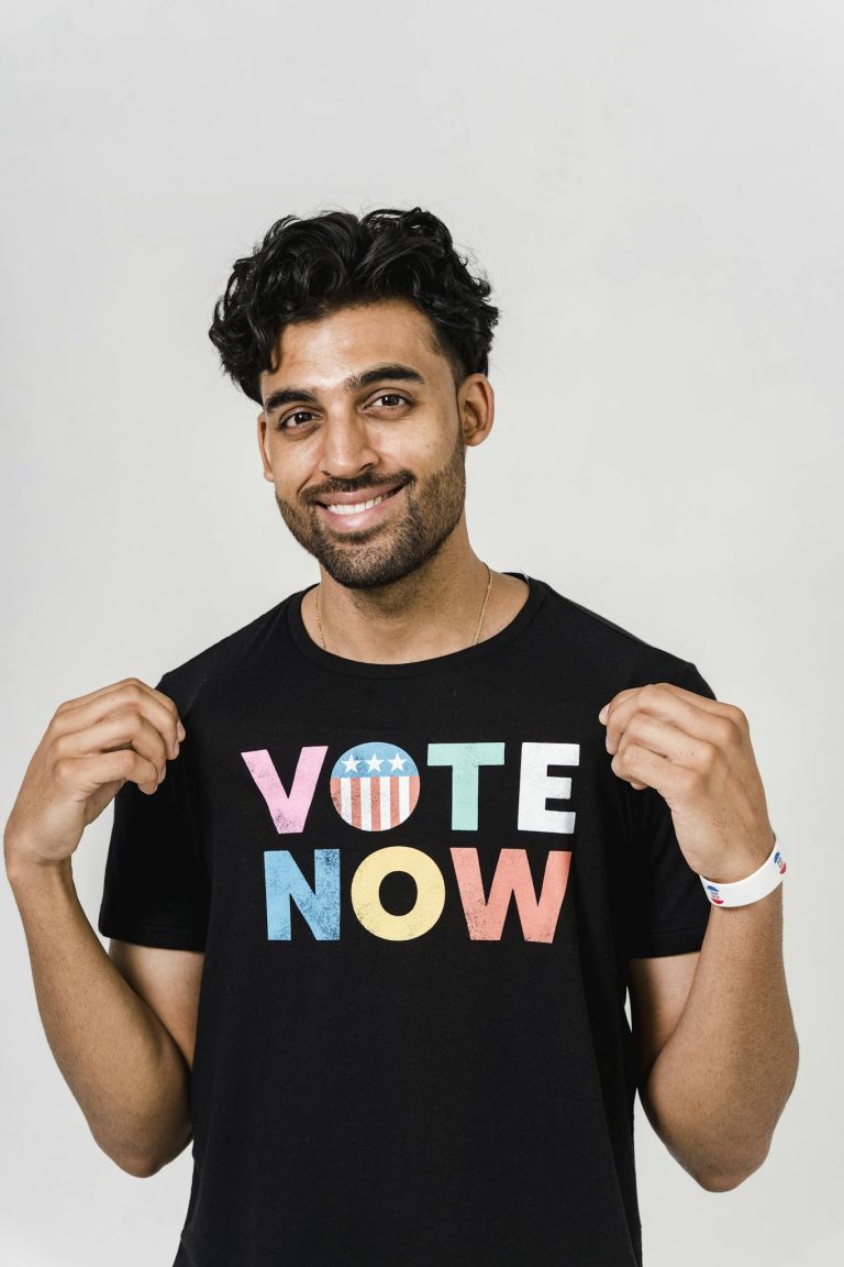 A smiling man in a vote-themed shirt encourages civic engagement.