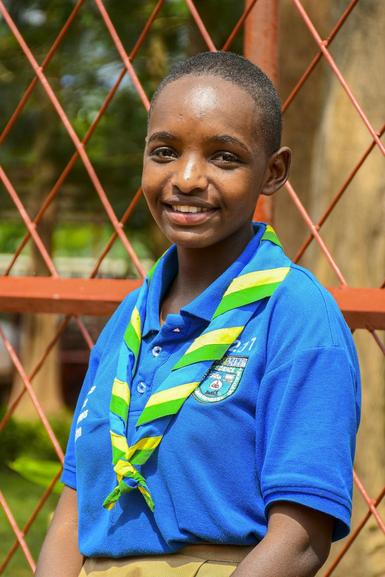 A young scout in a blue uniform poses outdoors in Southern Province, Rwanda.